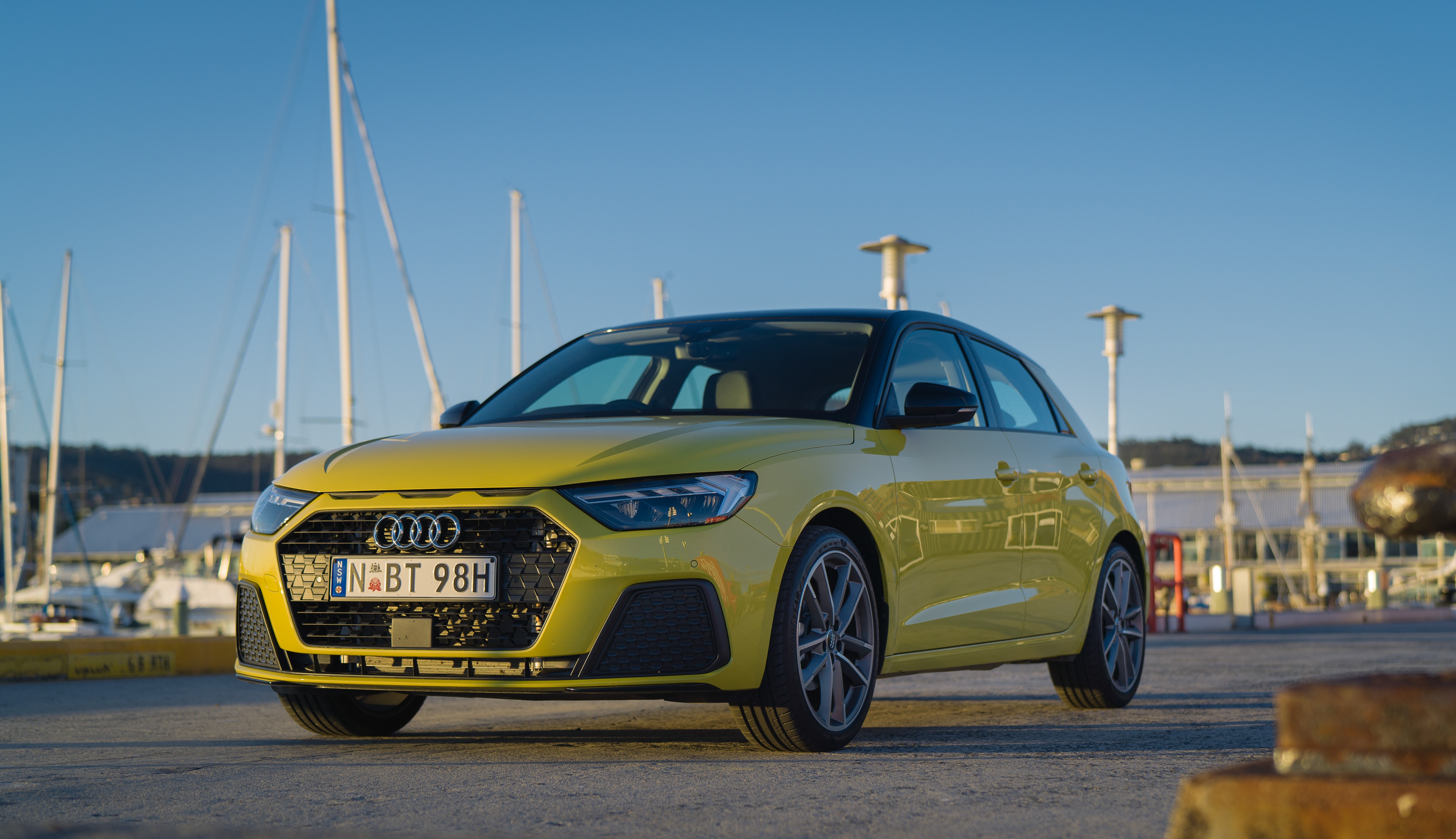 Yellow Audi A1 in front of boat harbour with clear blue skies