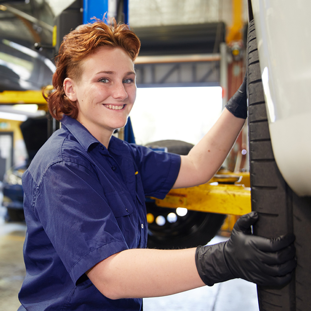 A young female RAC mechanic is checking a car tyre and smiling