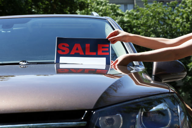 A sale sign being placed onto a car windscreen as part of a private sale