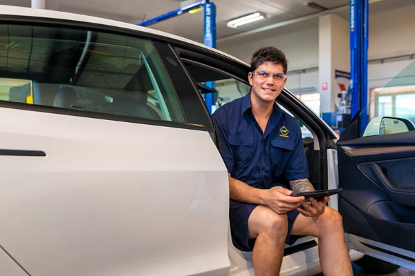 An RAC Auto Service mechanic seated in a Tesla performing maintenance checks using a digital tablet