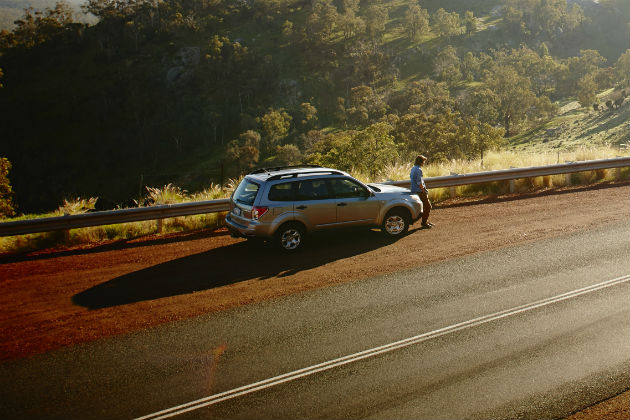 A driver sitting on the car bonnet on a rural road