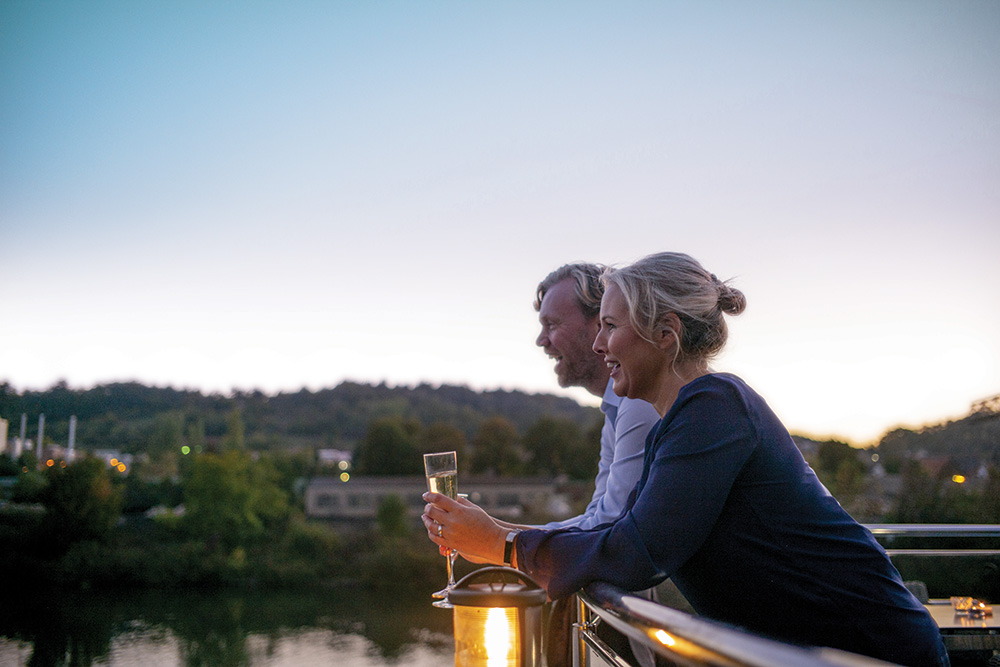 A couple leaning over a wooden railing with a glass of wine and enjoying each other's company