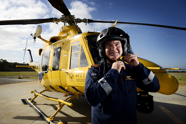 An RAC Rescue Pilot is putting on his helmet while standing in front of a yellow helicopter