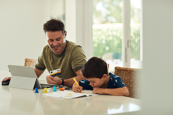 An RAC employee is working from home while a young boy is colouring in a book next to him