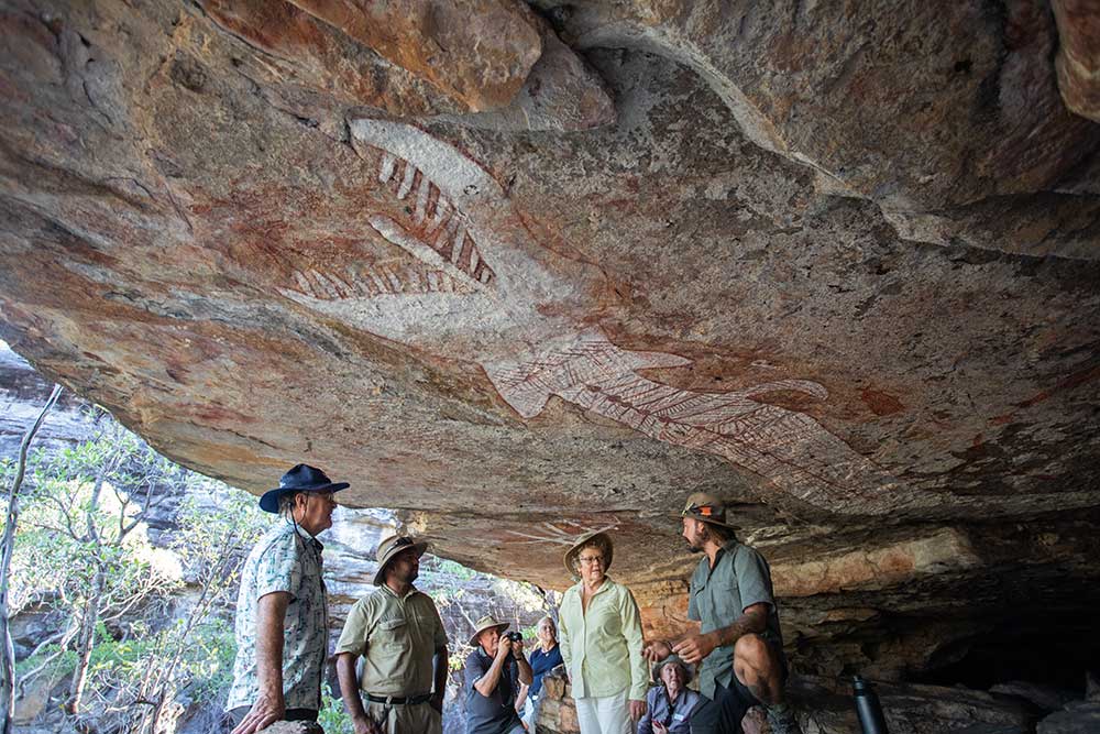 A tour guide is showing his guests an Aboriginal rock painting on the roof of a cave in Arnhem Land