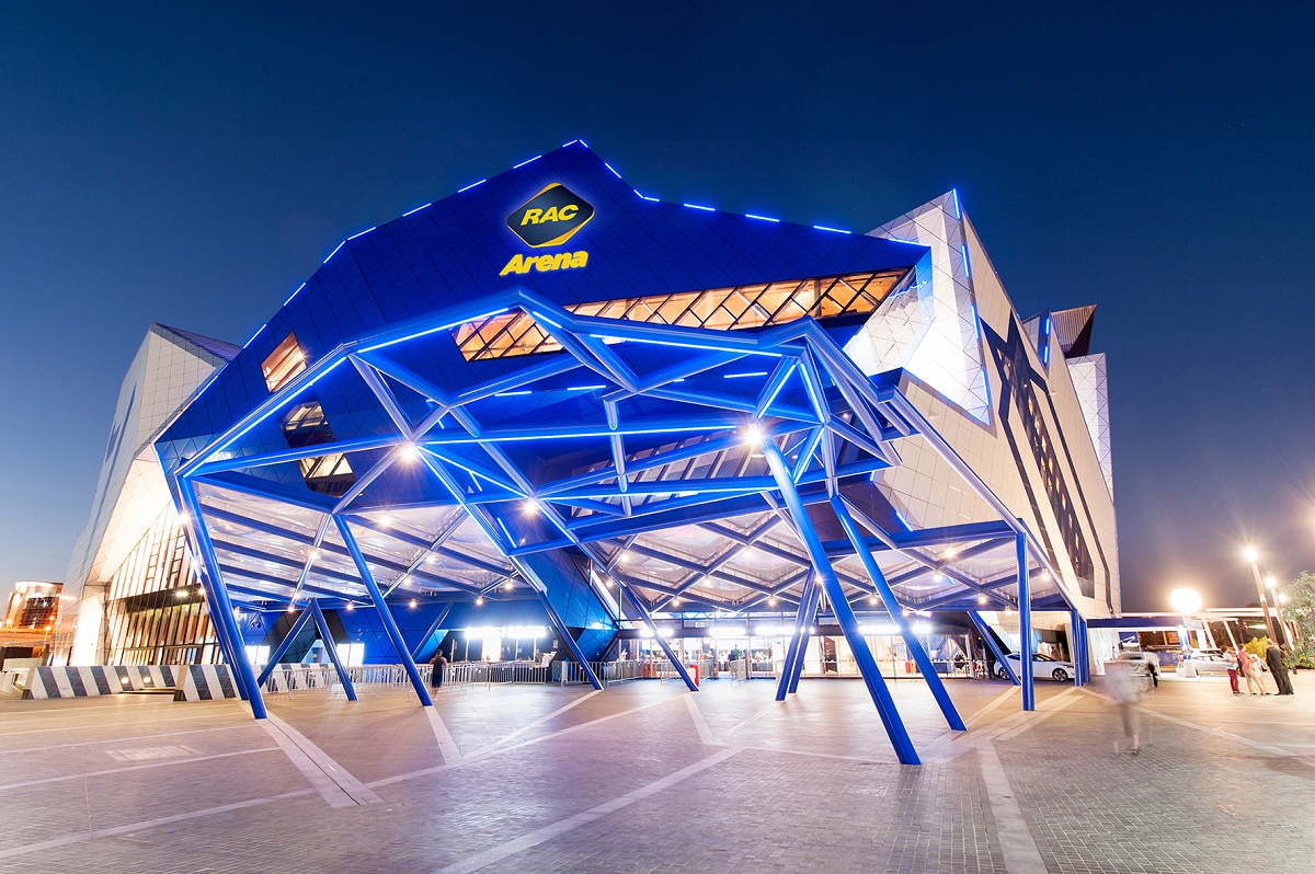 RAC Arena lit up at night with people walking past in a blur.