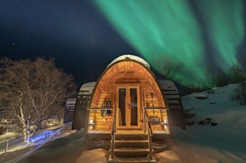 A snowhotel in the middle of a snowy landscape with Northern Lights glowing in the background 