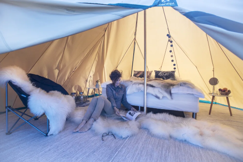 A woman is sitting on a furry rug inside your cosy tented cabin