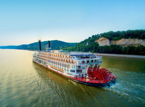 American Queen steamboat with its red paddlewheel cruising down the river
