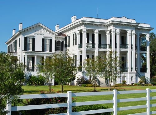 The front of a mansion in Nottoway which is an intricate building in white and black colours with a neat front yard and a white fence 