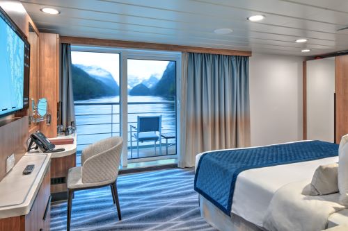 The interior of the stateroom aboard the American Queen Voyager with elegant furniture in blue and grey tones similar to the nature colours outside the balcony window