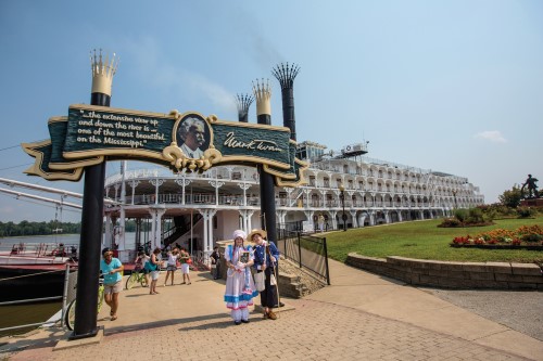 An arch dedicated to Mark Twain with a photo of him in the middle and the quote "the extensive view up and down the river is one of the most beautiful on the Mississippi" with the American Queen docked in the background