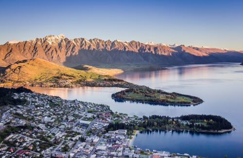 Sunset covering snowy capped mountains in light while the town of Queenstown is already in shade