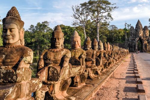 Path to a sandstone temple in Angkor Thom flanked by statues of gods with peaceful and happy expressions. 