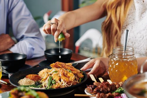 Close up of a woman squeezing some lime juice on top of an Asian dish