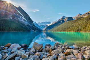 View of crystal-clear Lake Louise surrounded by towering mountains on a sunny day. 