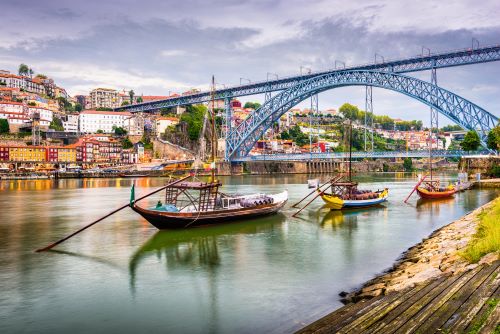 Three traditional Portuguese cargo boats with barrels lined up in the Douro River with the iconic bridge in the background