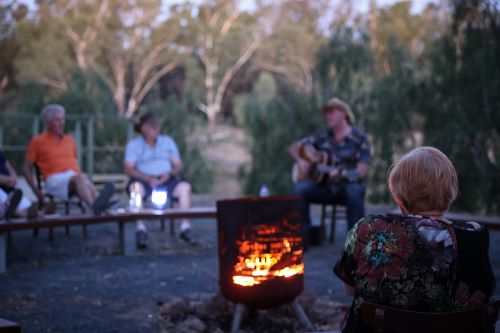 Some travellers sitting around the fire listening to a guitarist