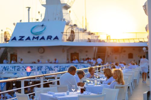 Passengers enjoying dinner on deck of an Azamara vessel with the sun setting in the background