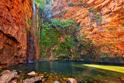 A stunning natural swimming hole surrounded by tall red cliffs and lush greenery.
