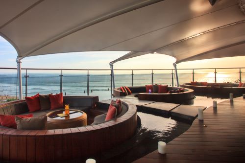 Three round seating areas with inviting cushions and a round table in the middle located at the rooftop of the hotel overlooking the ocean and beach at sunset