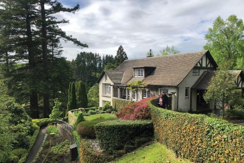 A couple standing outside their cottage and enjoying the views of a lush garden surrounded by trees. 