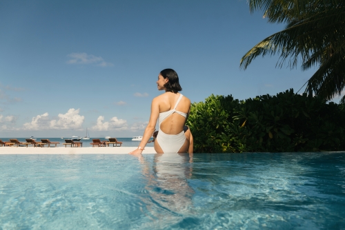 A woman sitting by the pool overlooking the beach.