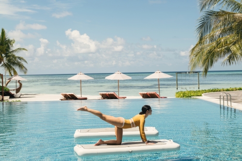 A woman practicing pool yoga on a floating mat with the ocean view in the background.
