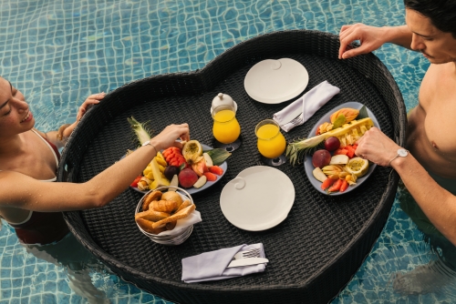 A couple enjoying a floating breakfast in the pool.