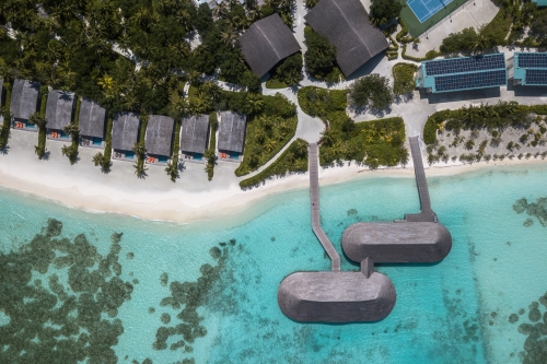Aerial image of the villas by the shore and two floating restaurants leading into the turquoise water.