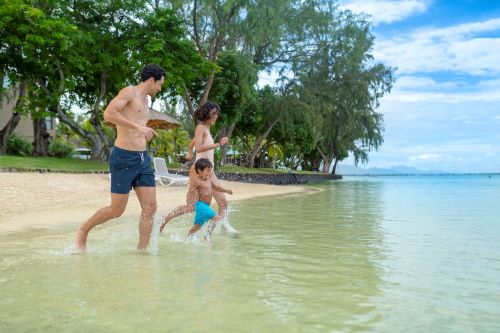 A couple with a young kid running from the beach into the calm water