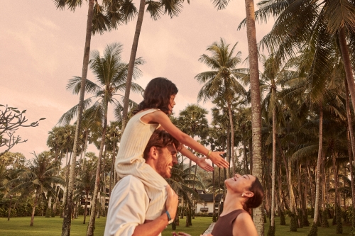 A family of three having fun at sunset with palm trees in the background