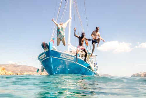 Young travellers jumping off a sailing boat into clear blue water