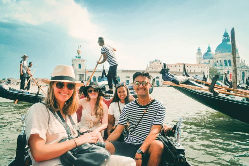 A group of young travellers sitting in a gondola with Venice and more gondolas in the background