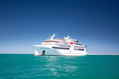 The Coral Adventurer vessel in the middle of the turquoise ocean towards a deep blue sky