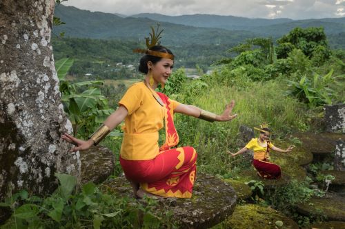 Two women wearing traditional yellow and red costumes and a headband while performing the Moyo dance squatting and spreading arms open like flying birds
