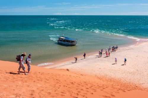 A tender boat at Point Peron letting people out on the orange sand beach which stands in high contrast to the blue ocean