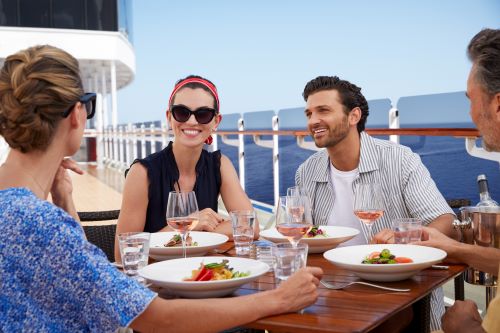 Two couples enjoying food and drinks on deck with the ocean in the background