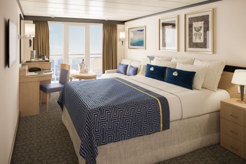 Interior of the Club Balcony stateroom with a big bed and lounge area all kept in shades of cream and blue