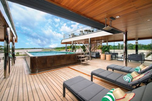 A luxurious outdoor deck with lounge chairs, a small pool, and scenic views under a sunny sky.