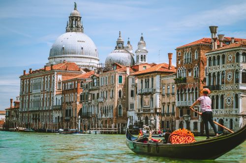 Gondola with Gondolier travelling through the Canals in Venice with St Marks Basilica in the background 