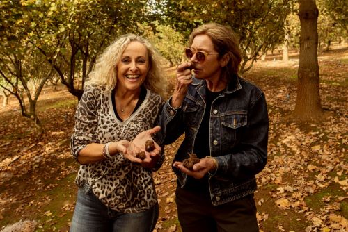 A couple of women standing in the forest smiling in the camera while holding and smelling some truffle