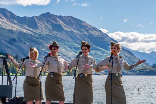 Four female pilots dressed in vintage attire performing in front of mountain and lake scenery 