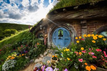 A Hobbit house with a bright blue door and many colourful flowers planted in the front yard
