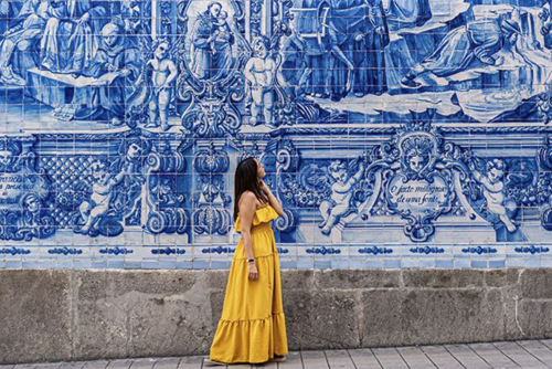 Woman in yellow dress walking along a blue tiled wall 