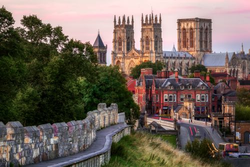 Part of the city wall in York in front of lush trees with a lookout to the cathedral and other historic buildings