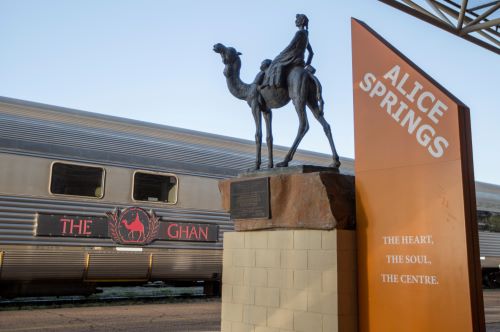 The Alice Springs train station sign with a statue of a woman riding a camel and The Ghan carriage in the background