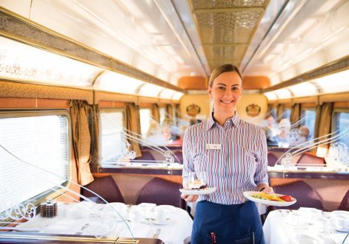 A waitress holding some plates with delicious food at the Queen Adelaide Restaurant aboard The Ghan