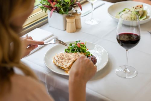 A closeup of a woman's dinner plate with a glass of red wine next to it