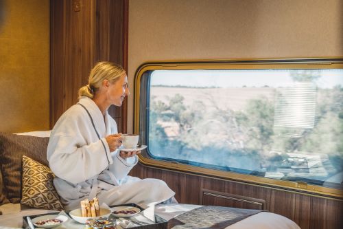 A woman enjoying a cup of coffee and looking outside the window while the train is passing the outback